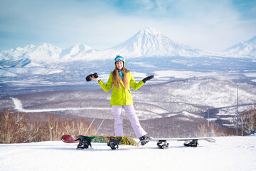 Cheerful girl snowboarder in green jacket in front of peaks snowy volcanos