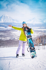Cheerful girl snowboarder in green jacket in front of peaks snowy volcanos