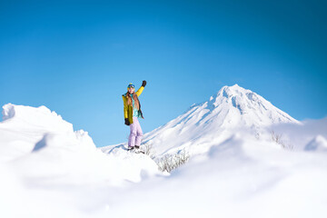 Naklejka na ściany i meble Cheerful girl snowboarder in yellow jacket in front of snowy mountains and blue sky