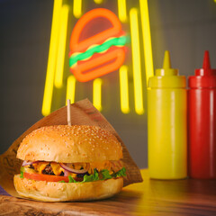 fast food concept of hamburger with two bottles of sauce on neon burger light in night cafe