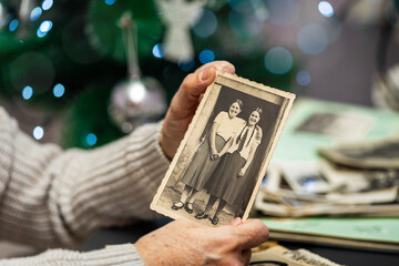 Old woman holding and old photo on Christmas tree background. Family and life values concept.