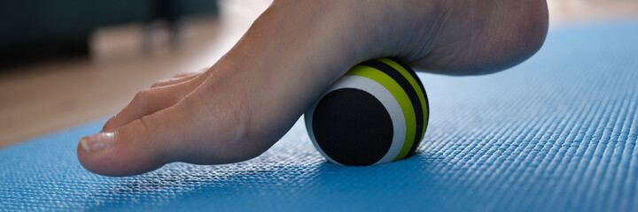 Woman leg rolling ball on foot at home closeup
