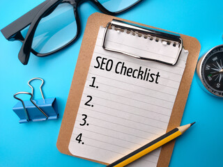 Glasses,pencil,compass and paper clips with text SEO Checklist on blue background.
