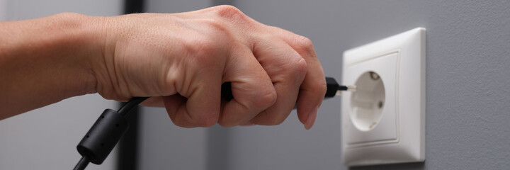 Woman hand inserts electrical plug into outlet closeup