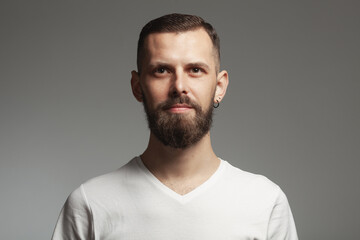 Fototapeta premium Male beauty concept. Emotive portrait of proud charismatic slim young bearded man posing over light gray background. Perfect haircut. Hipster style. Close up. Studio shot