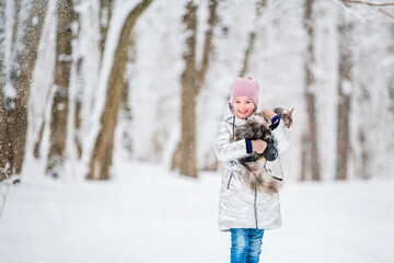 Fototapeta na wymiar little girl carries cat in her arms in a snowy winter