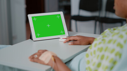 Close up of horizontal green screen on digital tablet in hospital ward. Sick patient looking at isolated background and mockup template with chroma key on gadget display. Technology