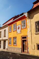 Kolin, Central Bohemia, Czech Republic, 10 July 2021: Narrow picturesque street with colorful renaissance baroque historical houses in medieval town center, sundial with the image of the sun
