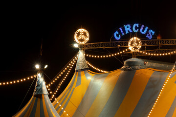 A circus tent at night with its colorful lights on

