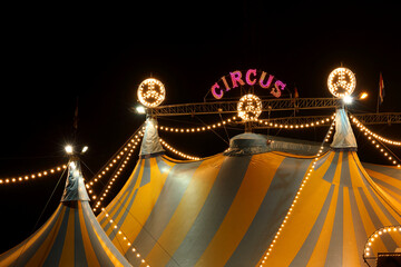 A circus tent at night with its colorful lights on
