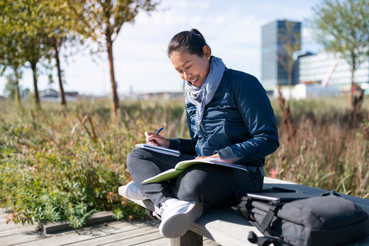 Young woman sitting on wooden bench and learning