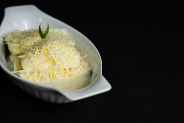 Singkong Thailand or called Thai sweet cassava serve with coconut milk and sprinkled with grated cheese on black background