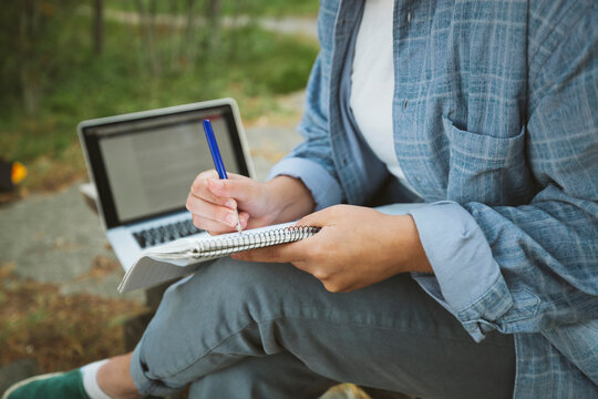 Young woman with notepad and laptop sitting on bench