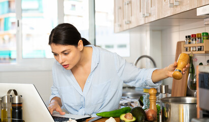 Nice woman planning to cook, looking for recipe on internet in her kitchen