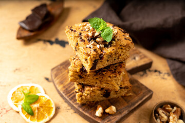 Pumpkin blondie bars with chocolate and walnuts close-up. Brownie pie slices on a serving wooden board on the dark culinary background. Baking for Thanksgiving	