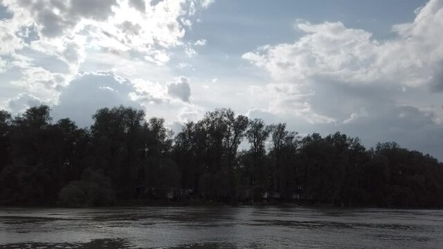 Steadicam shot from left side of sailing boat on the river with fishers huts on wooden pillars. Partly cloudy