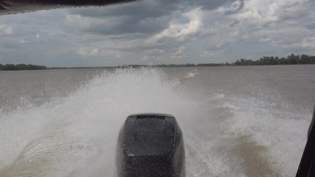 Steadicam shot from sailing speed boat stern on the river with engine and great splashes. Forest shores in distance. Partly cloudy