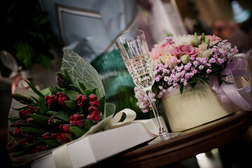On the table are bouquets of flowers and glasses of champagne on the background of gifts.