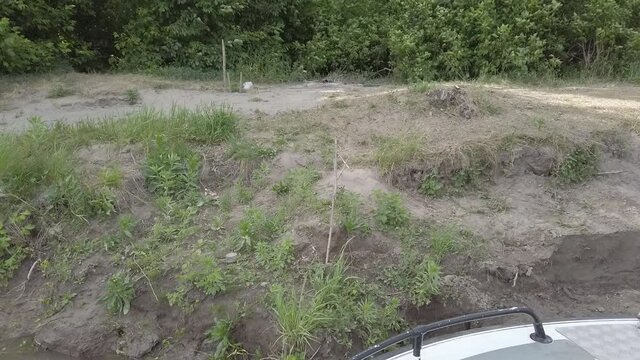 Steadicam shot from bow of motor boat leaves the shore with forest standing on it. Boat go sailing to the river with forest standing on the both shores and  water then. Weather is sunny, some sunbeams