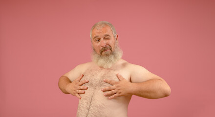 naked torso of a man with a gray beard, winks and covers the nipple with his hands on a pink background - obrazy, fototapety, plakaty