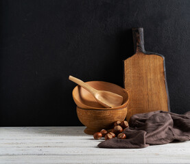 Wooden bowls and cutting boards on a wooden shelf against a rough plaster of a black wall. Rustic kitchen utensils.