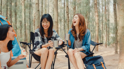 Group of young asia camper friends sitting in chairs by tent in forest. Teenager girl traveler relax and talk on a summer day at campsite. Outdoor activity, adventure travel or holiday vacation. © tirachard