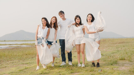 Portrait group of young multiethnical volunteers help to keep nature clean up looking at camera and smile with white garbage bags on beach. Concept about environmental conservation pollution problems.
