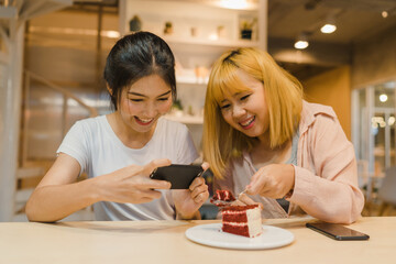 Obraz na płótnie Canvas Cheerful young Asia friend using phone taking a photograph food and cake at coffee shop. Two joyful attractive Asian lady together at restaurant or cafe. Holiday activity, or modern lifestyle concept.