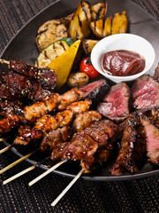 meat plate, set of different grilled skewers and grilled sliced filet mignon on a plate served with grilled vegetables, close up photo on a dark background
