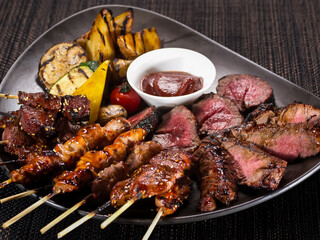 meat plate, set of different grilled skewers and grilled sliced filet mignon on a plate served with grilled vegetables, close up photo on a dark background