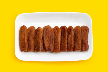 Sun dried bananas in white plate on yellow background.