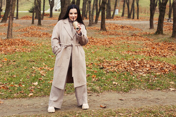 woman in a gray coat walking in the autumn park with a cup of hot drink