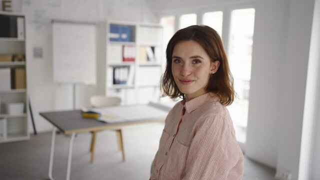 young woman sits in a bright modern office and looks to the camera