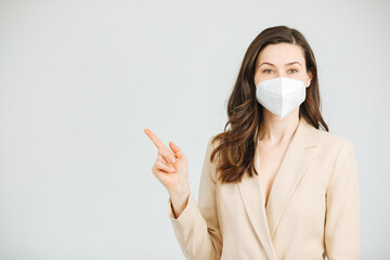 Businesswoman with FF2 mask shows something with her finger. With a mask at work during the pandemic. Working in the office with mask. Space for copy space 