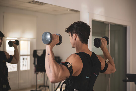 a young athlete lifts weights while wearing an electrostimulation vest.