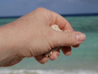A woman's hand holds a handful of fine white sand against the background of ocean waves on a sunny summer day on a summer vacation.