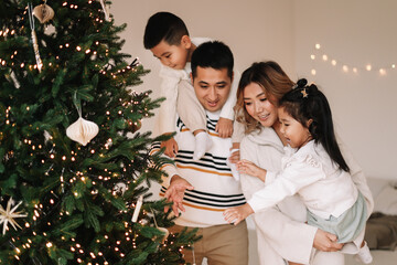 A happy diverse Asian family celebrates Christmas. Parents with children give gift boxes decorate the Christmas tree and prepare for the New Year holiday in a decorated house. Selective focus