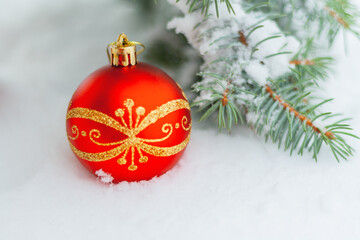 a beautiful red with gold ornament Christmas bauble lies on natural snow near a spruce branch