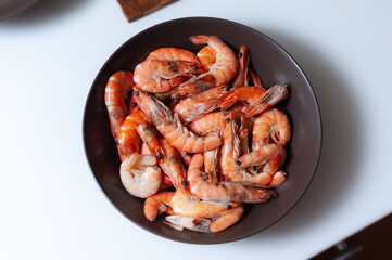 Unpeeled boiled shrimp in a dark plate on a white background
