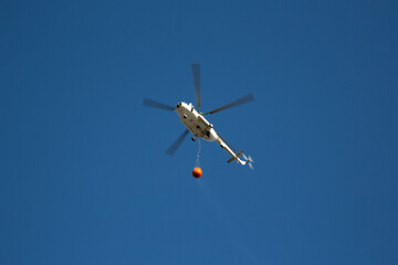 Helicopter going to fire area to extinguish forest fire.  Helicopter with a water bucket on a blue sky. One of the most effective ways to reach fire areas.