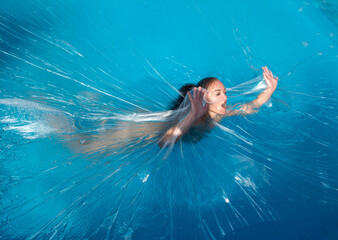 Young nude woman posing in polyethylene film under the water