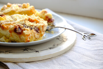 Two slices of homemade apple and apricot cheesecake pie with a beautiful stylish twig-shaped teaspoon on a wooden tray on a gray napkin on a white table. A healthy light lunch. Empty space.