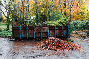 Big size metal skip in a park for fallen leaf and rubbish removal. Heavy industrial container to collect debris from a forest park on a specially designated area. Fall autumn season.
