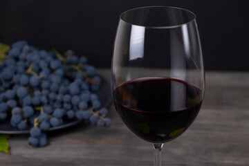 Composition with a glass of red wine and grapes on a dark background of gray wooden boards. Winemaking concept. Still life with wine in a dark key