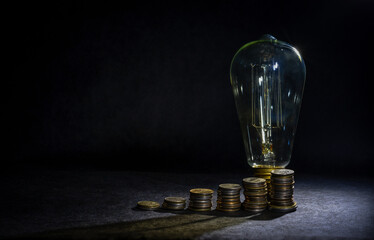 Columns of coins in the form of a growing diagram and an extinguished incandescent lamp on a dark...