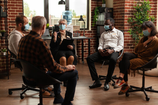 Specialist Giving Counseling To People At Aa Meeting During Pandemic. Woman Therapist Talking To Patients With Anger Problems And Addiction, Having Face Masks At Group Therapy Session.