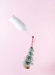 A glass of champagne flies with a Christmas tree. New Year aesthetic celebration creative concept on a pink background.