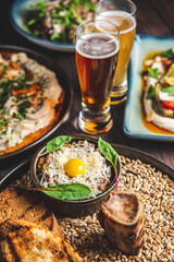 Close up of beef tartare served with two glasses of beer, one big potato pancake and baked zucchini.