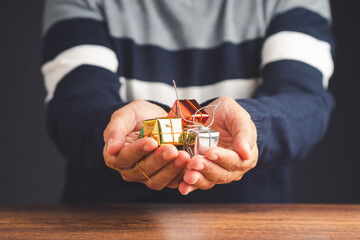 Christmas decorations in hands a young man in a sweater. Close-up photo. Small colorful gift boxes for decor the Christmas tree
