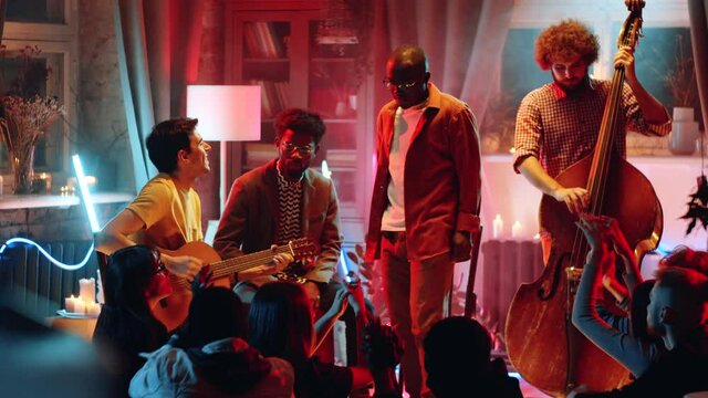 Multiethnic boy band playing live music and singing a song while giving concert in studio with neon light